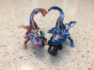 Two dragon sculptures: one has a wreath of flowers on her head, the other is taking a bite out of his top hat. Their tails curl together to suggest a heart.